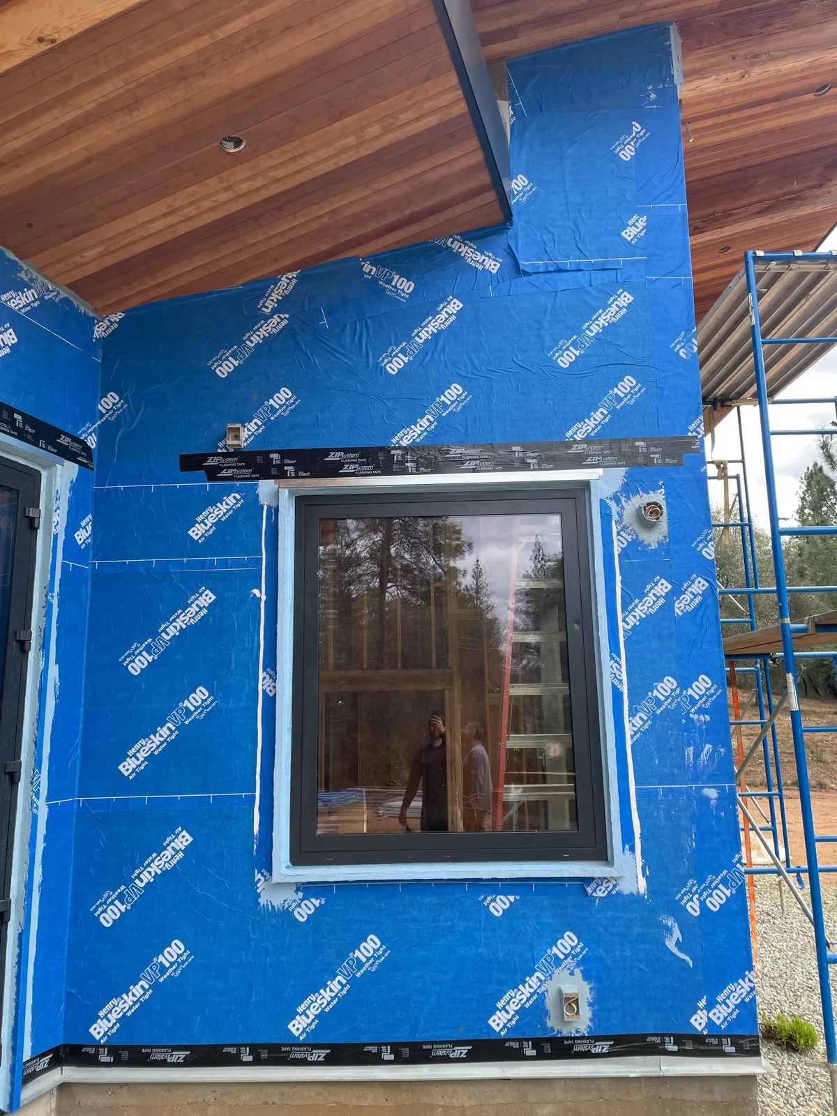 Window opening set in a blue weather-resistive barrier under a wood soffit