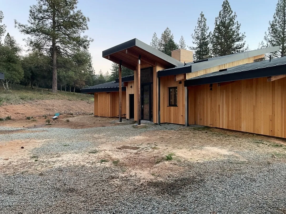Completed house with sugar pine siding and a tall covered entry, seen across a gravel drive